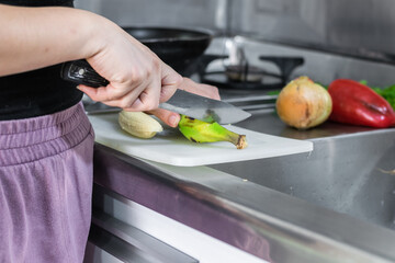 detailed view of the hands of a latina girl cutting a green banana with a knife on her kitchen cabinet