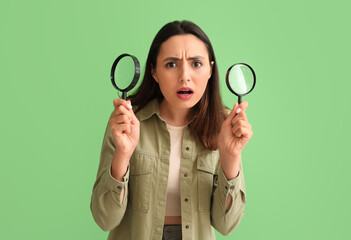 Upset young woman with magnifiers on green background