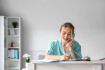 Female medical intern talking by telephone at reception in clinic