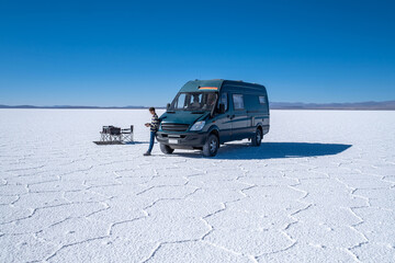 Boy leaning against his motorhome with his picnic equipment in the middle of a salt flat.
