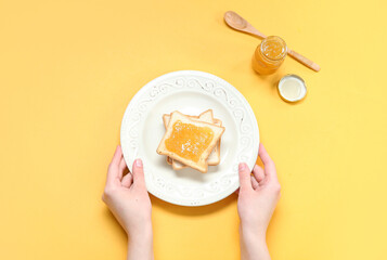 Female hands with plate of tasty toasts and jam on color background