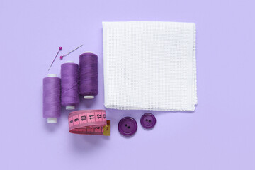 Canvas with buttons, thread spools and measuring tape on lilac background