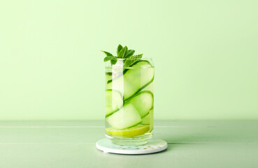 Glass of infused water with cucumber slices on green wooden table