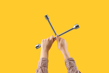 Female hands holding cross wrench on yellow background