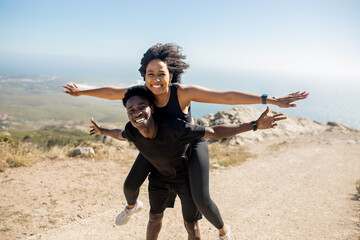 Happy black couple enjoying workout outdoors, man giving piggyback ride to woman and having fun by...