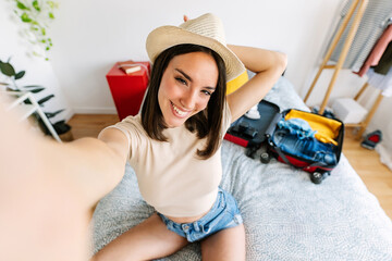Beautiful young woman traveler taking selfie portrait with phone while preparing summer vacation...