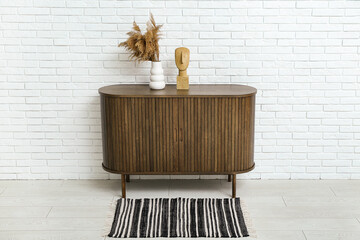 Wooden chest of drawers with pampas grass and decor near light brick wall in room