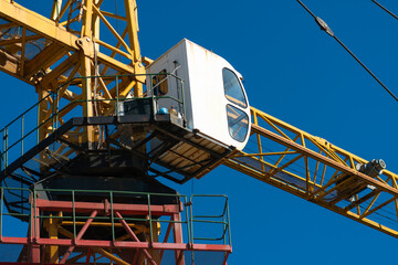 Close-up of a white operator's cabin on a yellow construction crane against a blue sky background