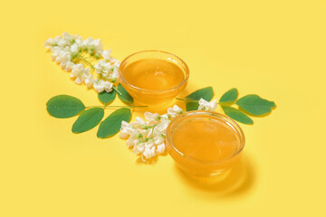 Bowls of honey with flowers of acacia on yellow background, closeup