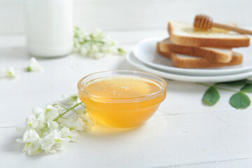 Bowl of honey with flowers of acacia and toasts on light wooden table, closeup