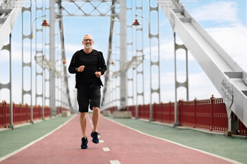 Fototapeta na wymiar Happy mature man jogging outside by bridge
