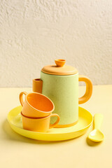 Plate with cups, teapot and spoon for baby on yellow table