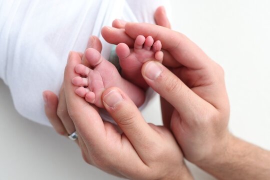 The palms of the father, the mother are holding the foot of the newborn baby on white background. Feet of the newborn on the palms of the parents. Photography of a child's toes, heels and feet.