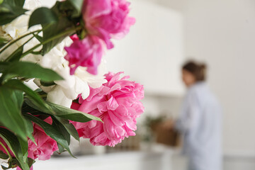 Bouquet of blooming peony flowers in kitchen with woman cooking dinner, closeup