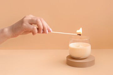 Woman lighting candle on pale orange background