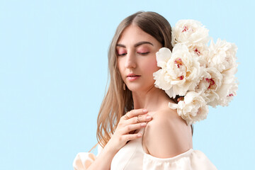 Beautiful young woman with bouquet of peony flowers on blue background