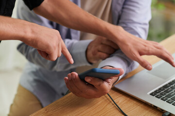 Hands of young man showing father how to transfer files from smartphone to laptop