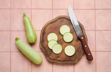 Wooden board with fresh zucchini on beige tile background