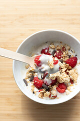yogurt bowl with cereal granola, oatmeal, raspberries and berries with natural wooden spoon