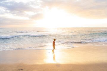 Horizontal image of a young man walking alone on the beach on a summer day with beautiful sunset...