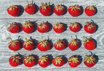 Strawberry crop on gray wooden table background in rustic style. Berries arranged in rows, view from above.