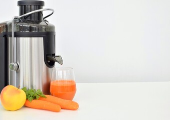 Freshly squeezed carrot-apple juice in a glass near a juicer, next to fresh carrots and an apple.  Free space for text.
