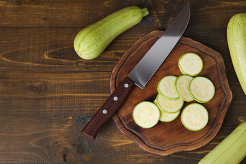 Board with slices of fresh green zucchini on wooden background