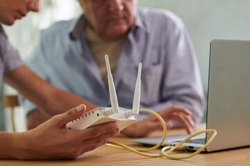 Closeup image of young man setting wi-fi router in apartment of his senior father
