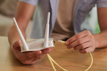 Hands of man inserting ethernet cord in wi-fi router