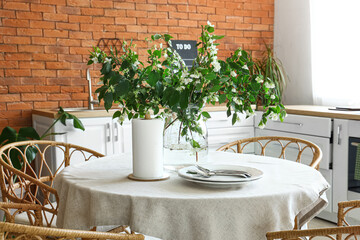 Vase with blooming jasmine flowers on dining table in kitchen