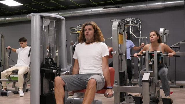 Concentrated adult man performing strength training in modern gym, doing presses for triceps in exercise machine. High quality 4k footage