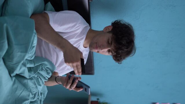 Arabic man using mobile banking holding smartphone and credit card in bed at home. Online shopping application concept.