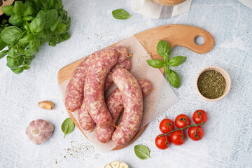 Wooden board with raw homemade sausages on light background