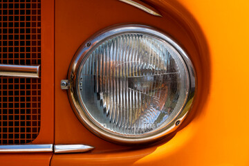 Headlight of a historic Oldtimer truck in bright sunlight. Orange livery with intense colorful...