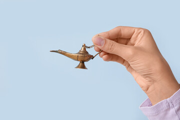 Young Muslim woman with Aladdin lamp on blue background, closeup. Islamic New Year celebration