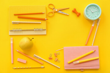 Frame made of alarm clock, fresh apple and different stationery on yellow background