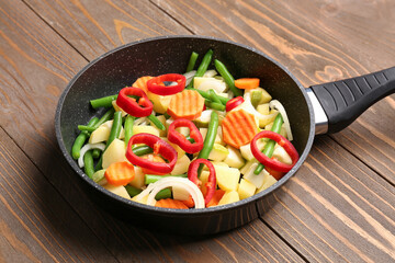 Frying pan with fresh vegetables on wooden background