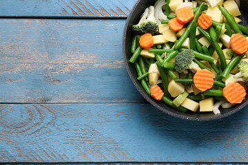 Frying pan with fresh vegetables on blue wooden background