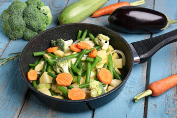 Frying pan with fresh vegetables on blue wooden background