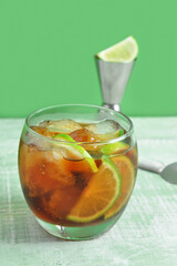 Glass of cold Cuba Libre cocktail on green wooden table