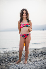 smiling girl in red swimsuit stands on the beach and holding sand ice-cream in her hand