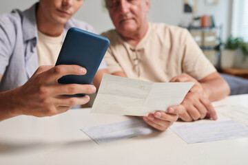 Young man helping grandfather to pay utility bills via mobile application