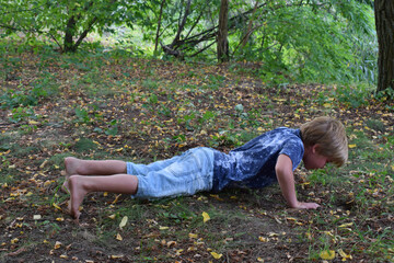 The boy performs a strength exercise in the forest.