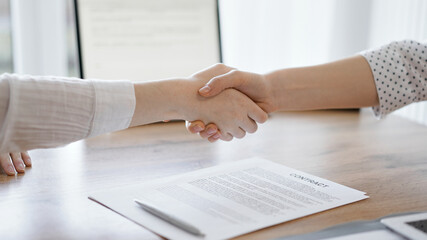 Obraz na płótnie Canvas Business people shaking hands above contract papers just signed on the wooden table, close up. Lawyers at meeting. Teamwork, partnership, success concept
