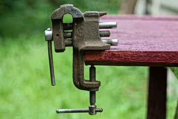 small iron rusty mechanical very old dirty retro vise for working with metal stands on a brown desktop on the street during the day