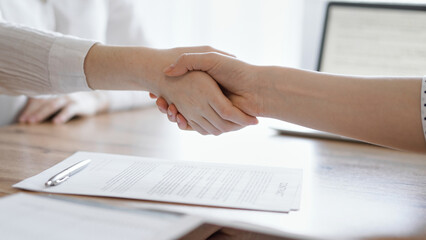 Business people shaking hands above contract papers just signed on the wooden table, close up. Lawyers at meeting. Teamwork, partnership, success concept