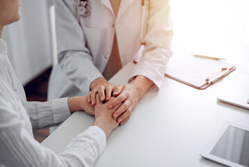 Doctor and patient sitting at the desk in clinic office. The focus is on female physician's hands reassuring woman, close up. Perfect medical service, empathy, and medicine concept