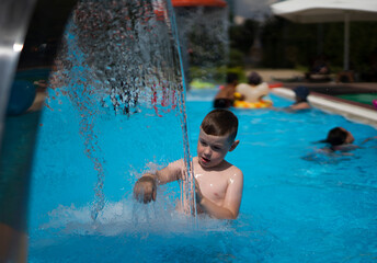 A blond boy of seven years old plays in the water of the pool in summer.