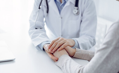 Doctor and patient sitting at the table in clinic office. The focus is on female physician's hands reassuring woman, only hands close up. Medicine concept