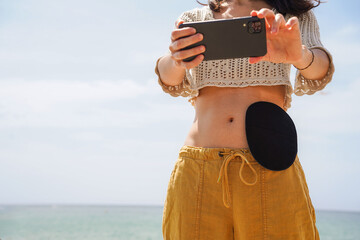 unrecognizable woman with a black ostomy bag taking a selfie in the beach. Colostomy of a colon...